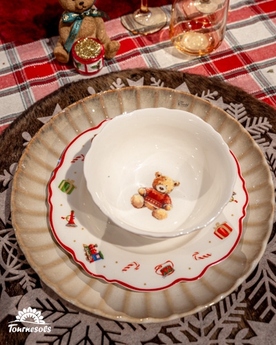 Assiettes superposées avec motifs de Noël et un ourson sur nappe à carreaux.